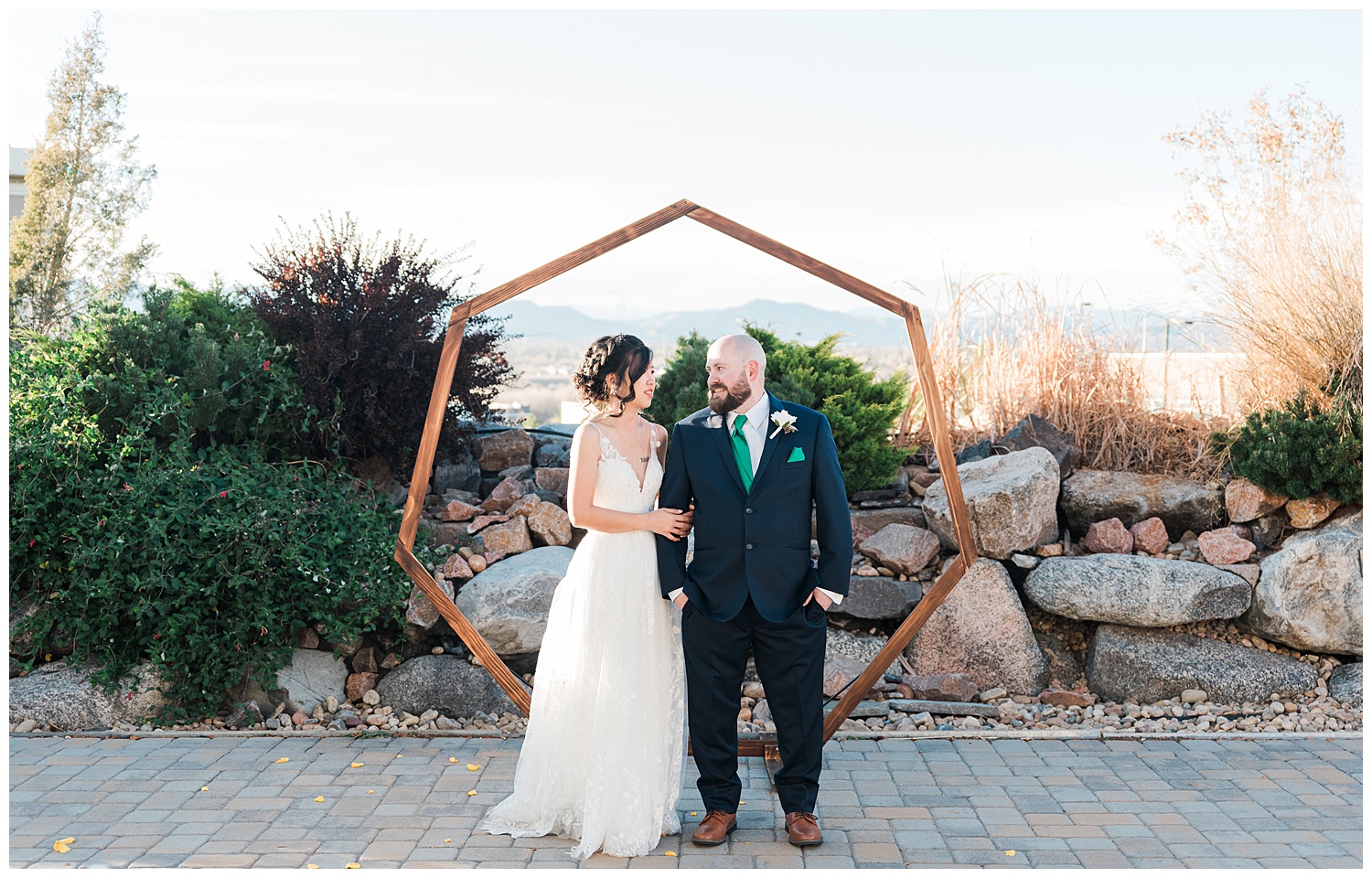 Bride and groom stand arm in arm at their wedding alter in front of a hexagonal arch at Ashley Ridge, an outdoor castle rock wedding venue