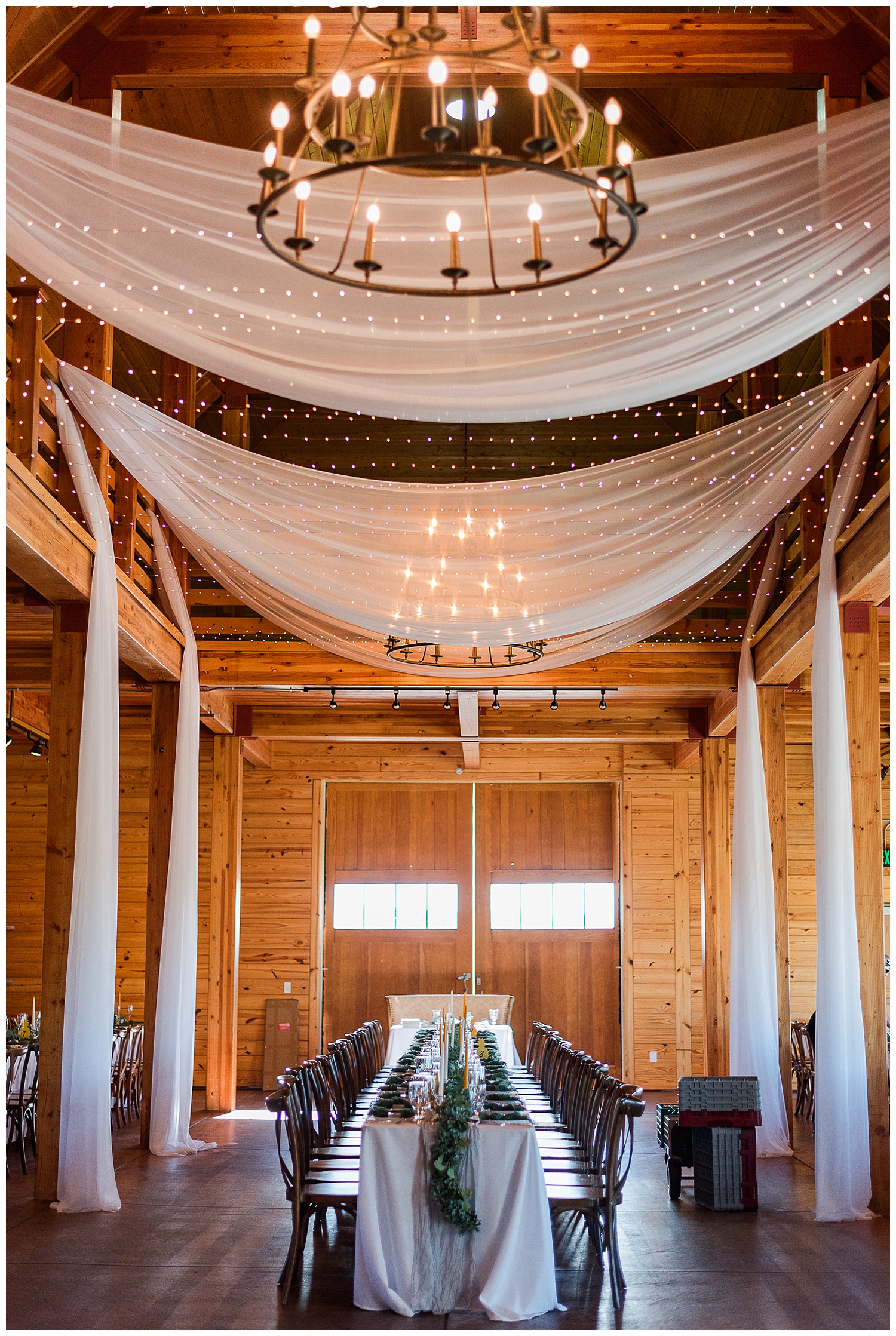 A vertical photo of the reception barn space with tables set up ready for the reception