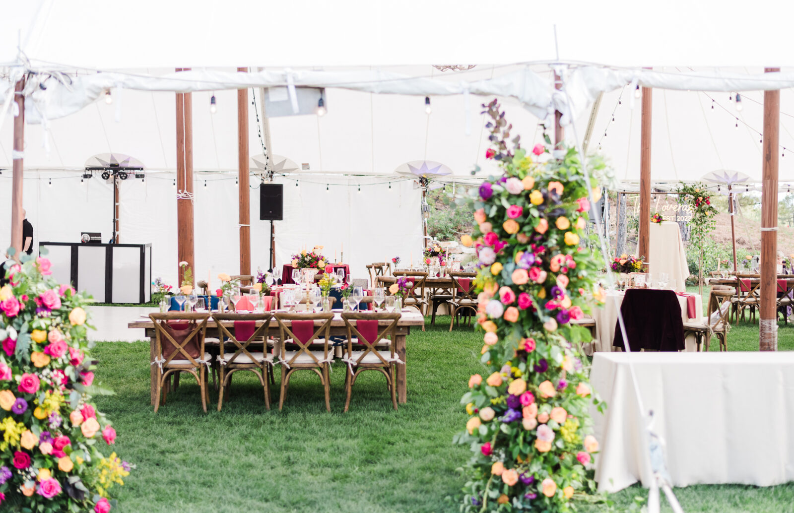 A photo of a table at a reception with red velvet chairs and a large flower display in an outdoor tent for on the golf course at Castle pines, a castle rock wedding venue