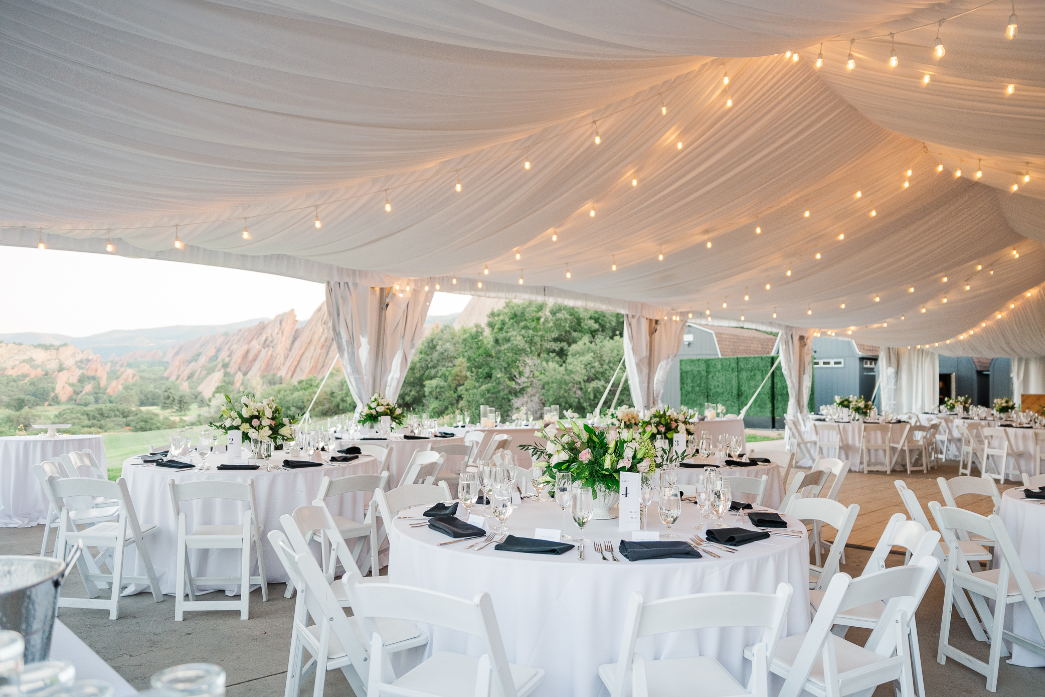 Milk Glass Productions, a beautiful wedding planning company sets up an outdoor ceremony site inside a white tent with white table cloths and florals