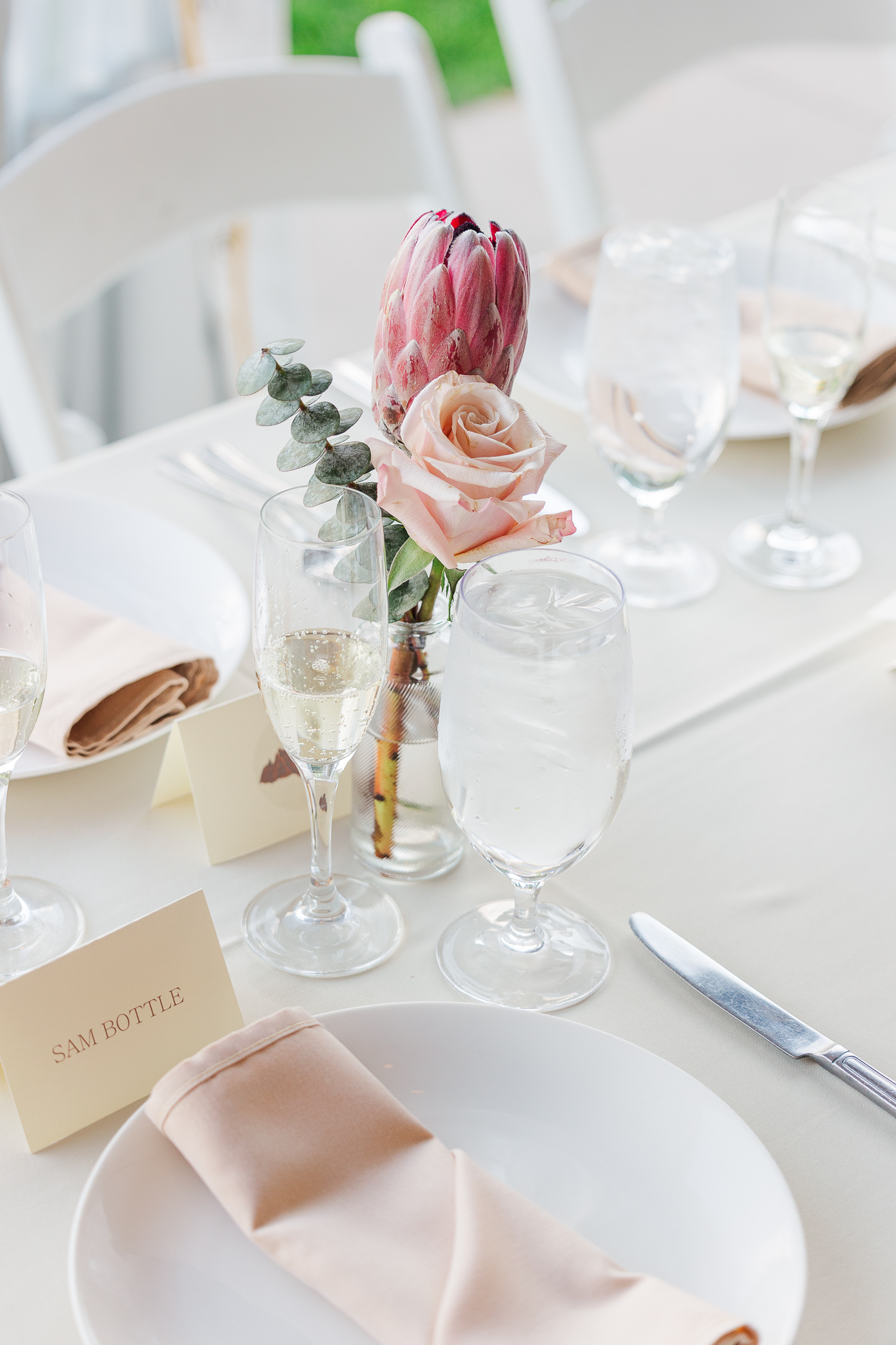 Details of floral centerpiece with 2 pink flowers and 1 greenery piece with plates and cups around it as well as dusty pink napkin on the plate, with the help of Calluna Events