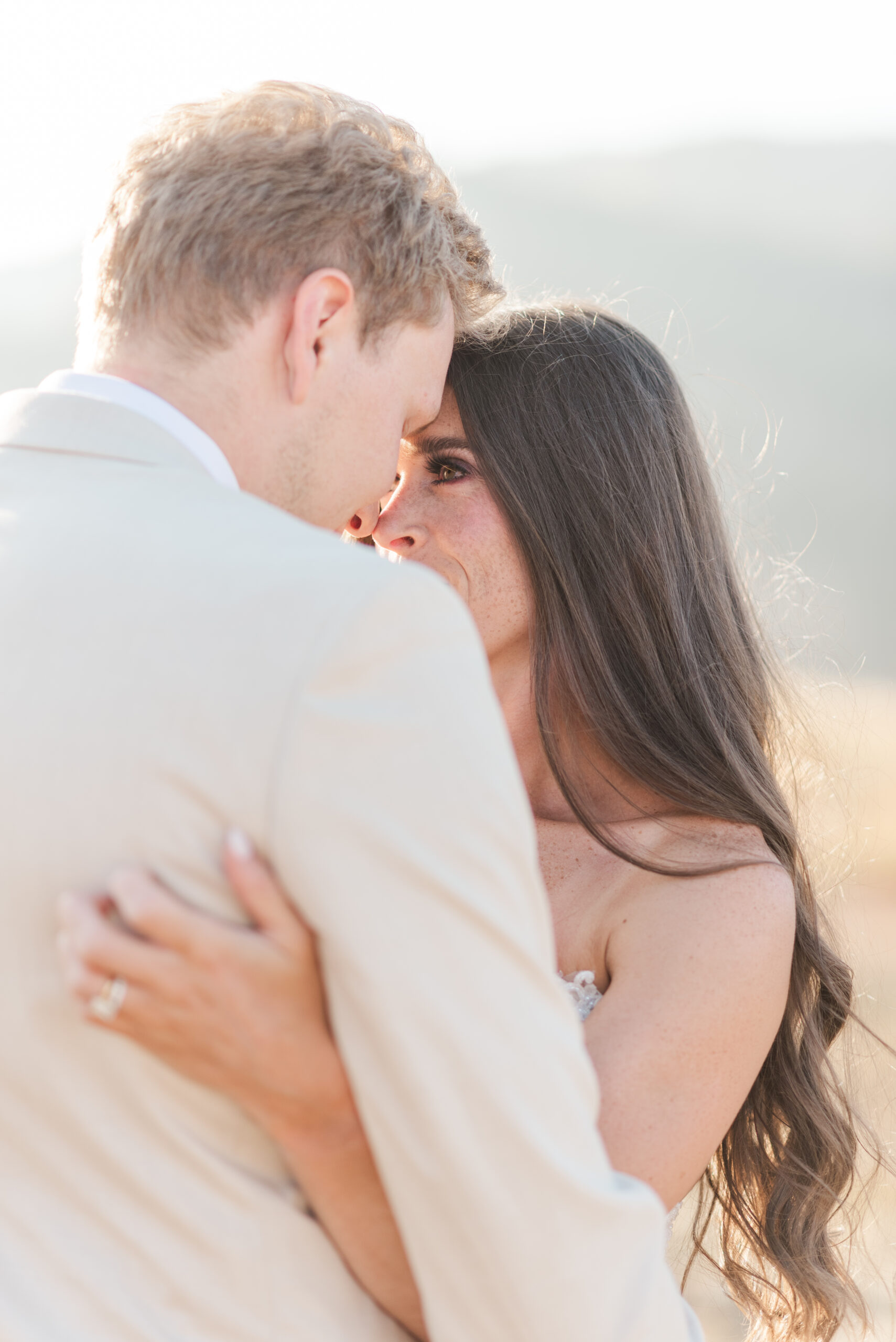 A bride and groom embrace with a close up on the bride's face and her hair down and long forehead touching her groom in a tan suit planned with Colorado wedding planners