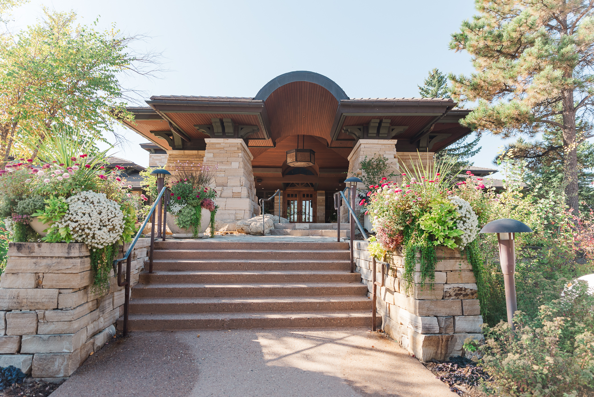 The entrance to Sanctuary Golf Course Wedding Venue is line with tan bricks, stairs, and beautiful flowers and trees around the space.