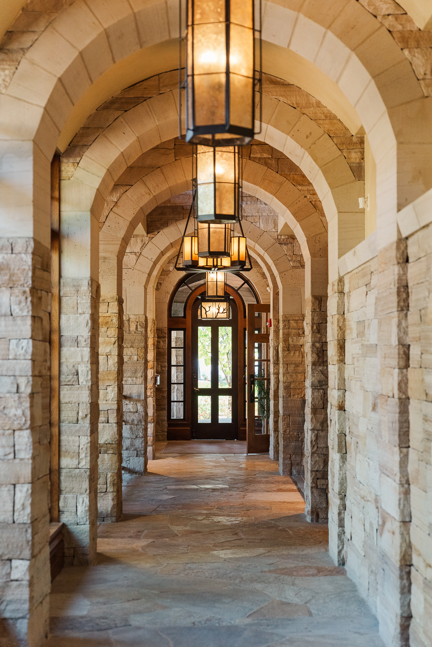 A hall in a wedding venue with rounded ceiling and beautiful sconces on the ceiling complete with white stones walls, ceiling, and floor.