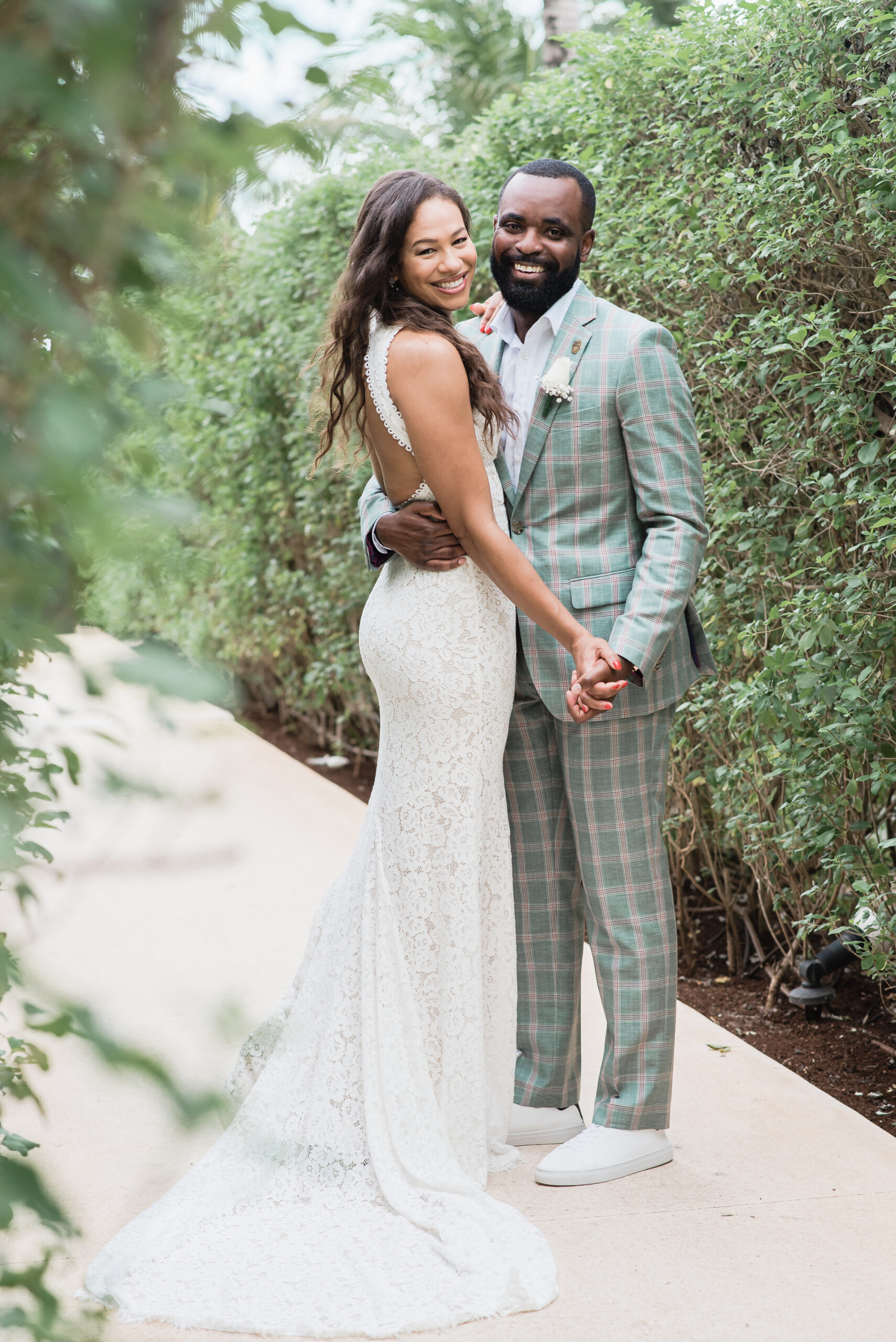 A bride and groom smile towar the camera while on a sidewalk path lined with green bushes at St. Julien Hotel Wedding