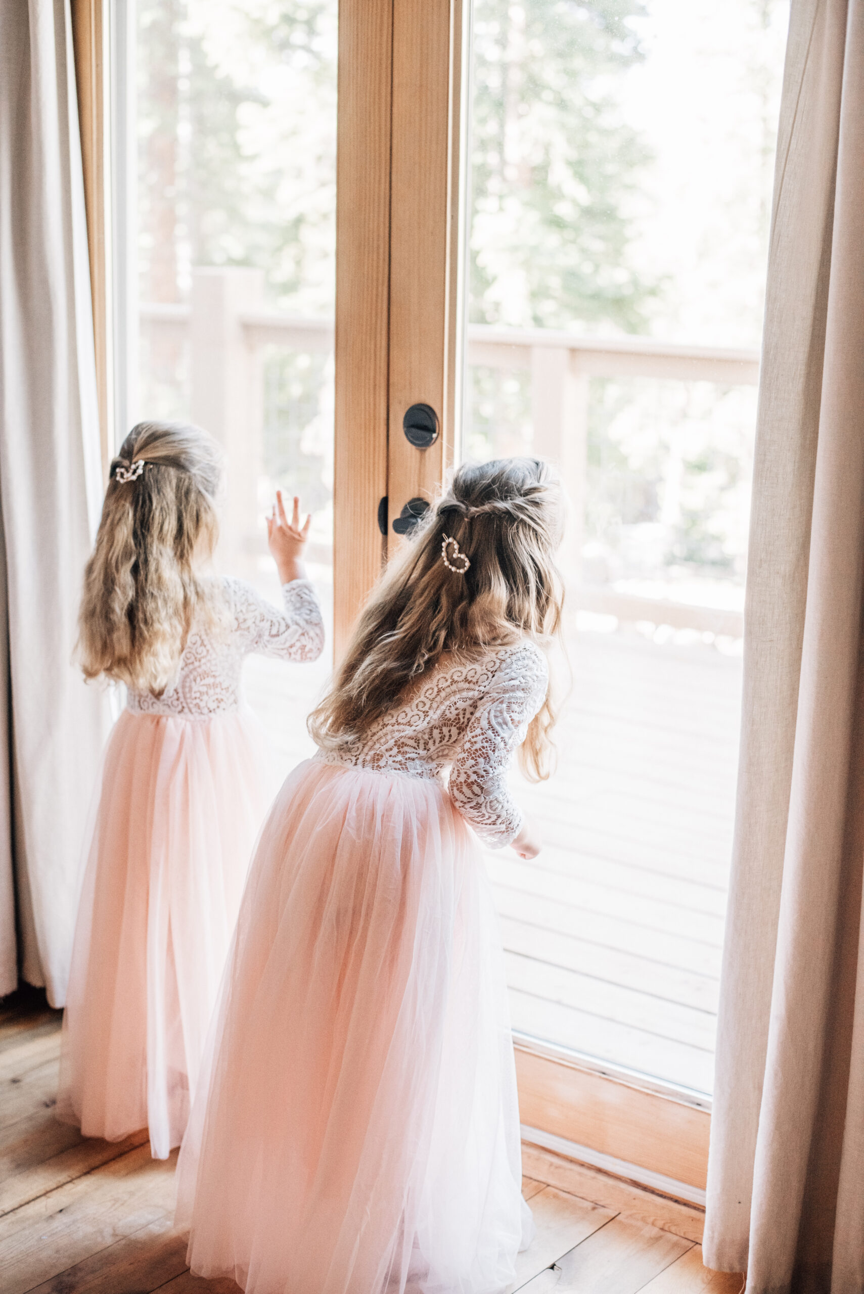 Two little girls look out a large glass door in their flower girl dresses at a Granby Ranch Wedding