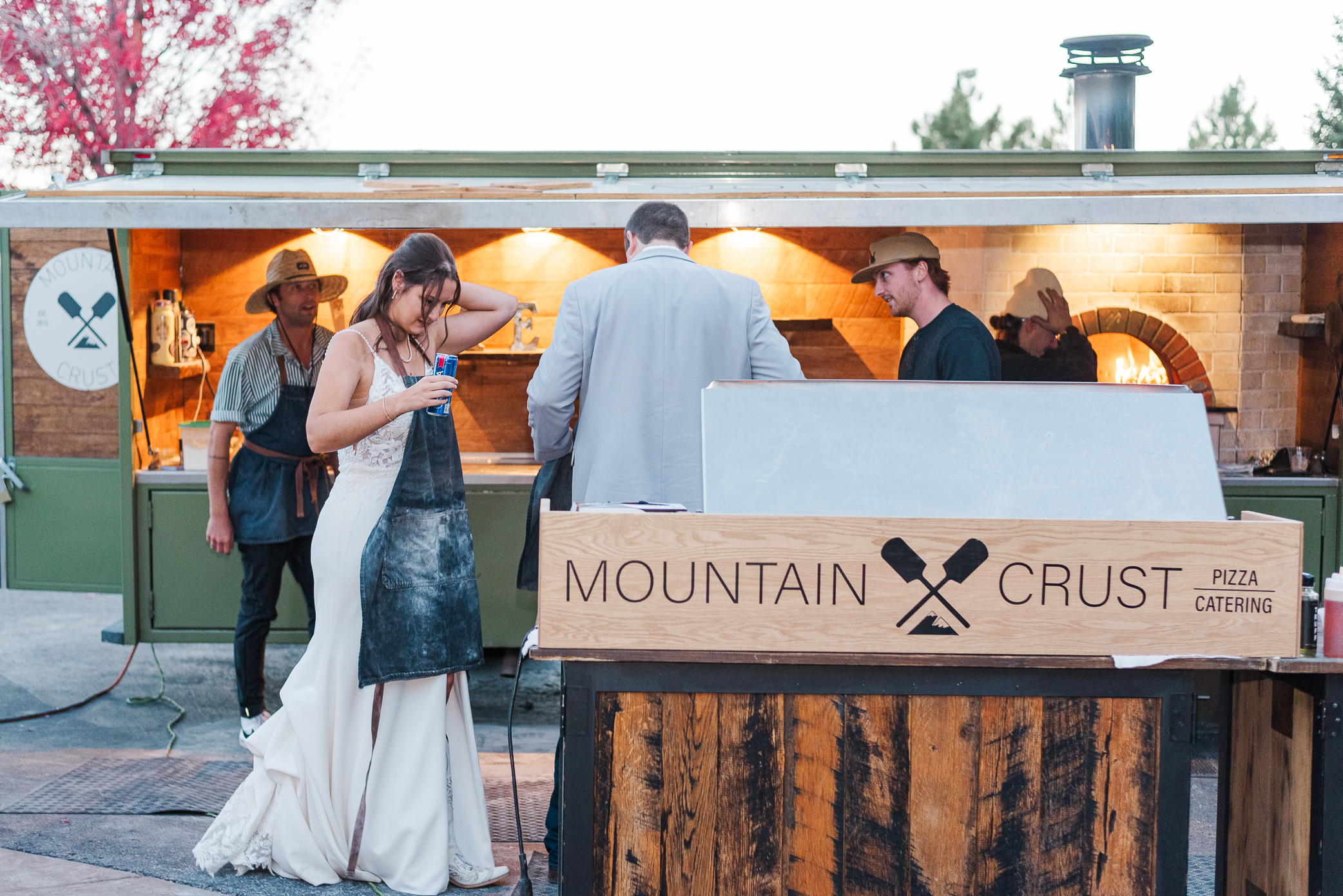 Mountain crust event venue photo of the sign and a bride putting on her apron to cook pizza on their wedding day