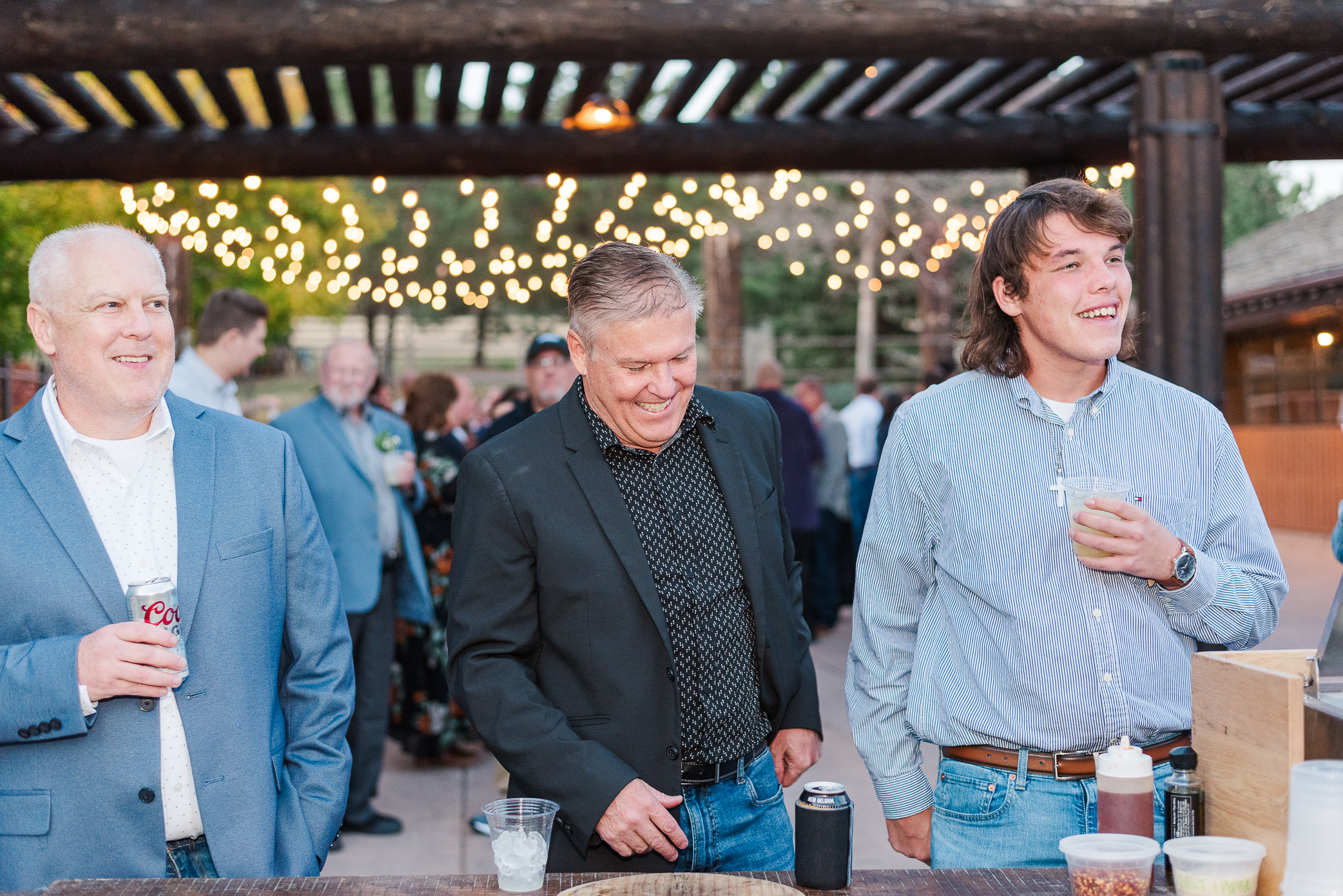 Three men at a wedding in nice clothes smile at the events happening at the wedding day off camera