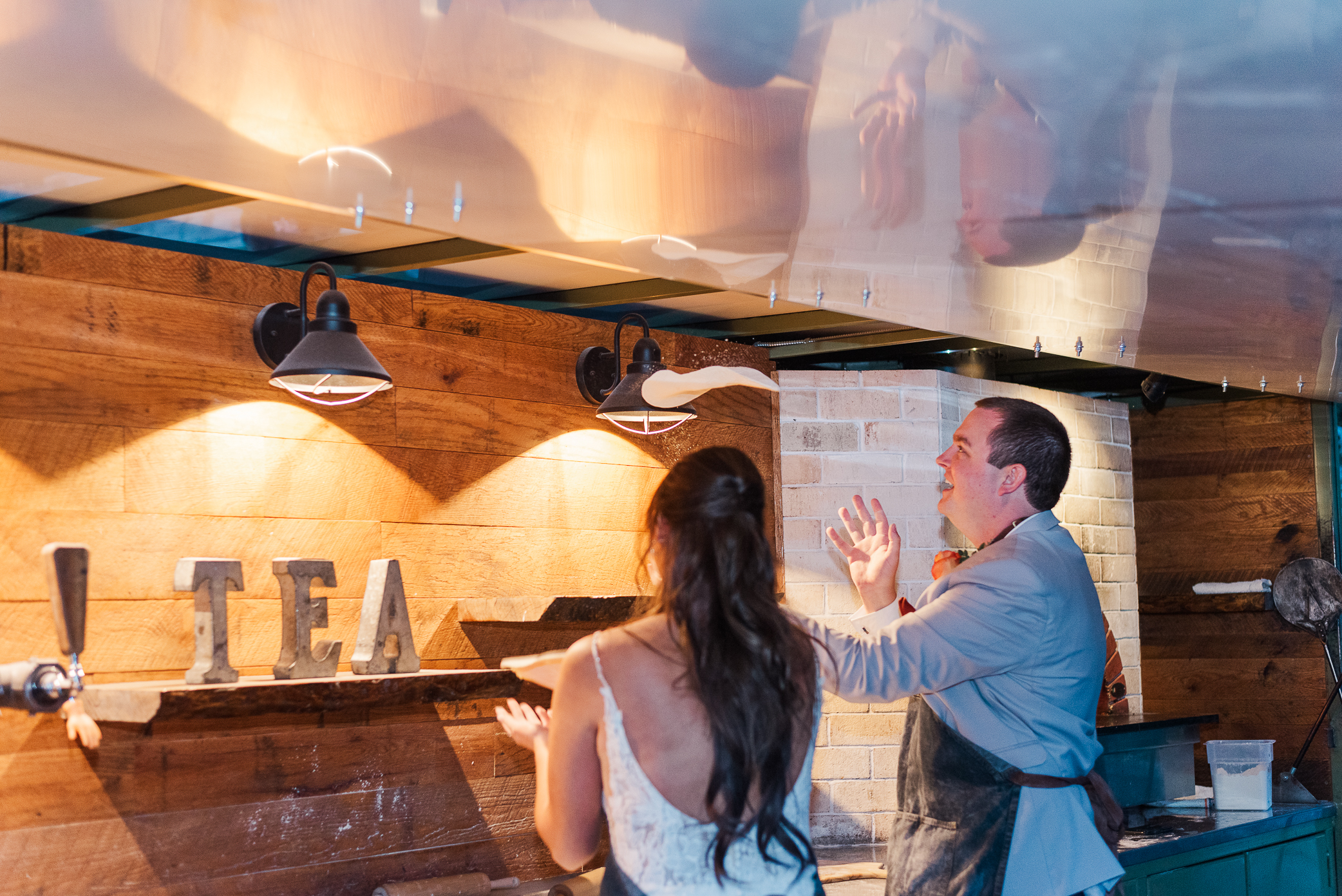 A groom tosses pizza dough into the air at Mountain crust event venue on his wedding day with his wife-to-be standing next to him