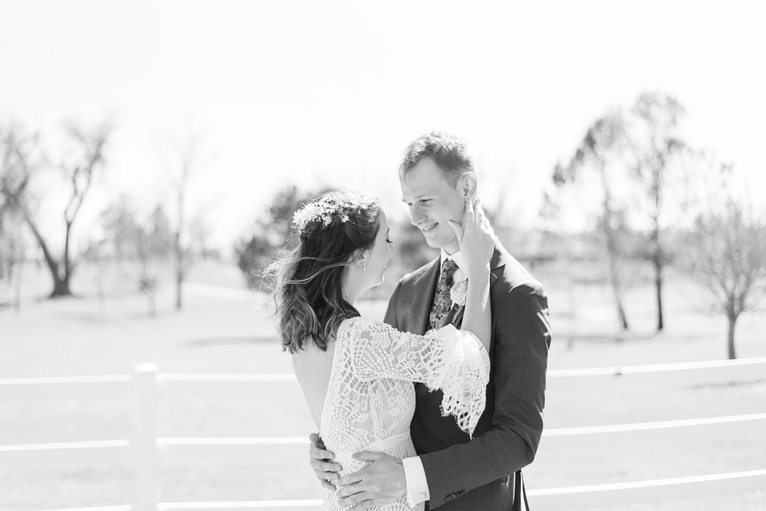 A groom wraps his arms around his new bride as the bride smiles and he looks at her and they share an embrace. 